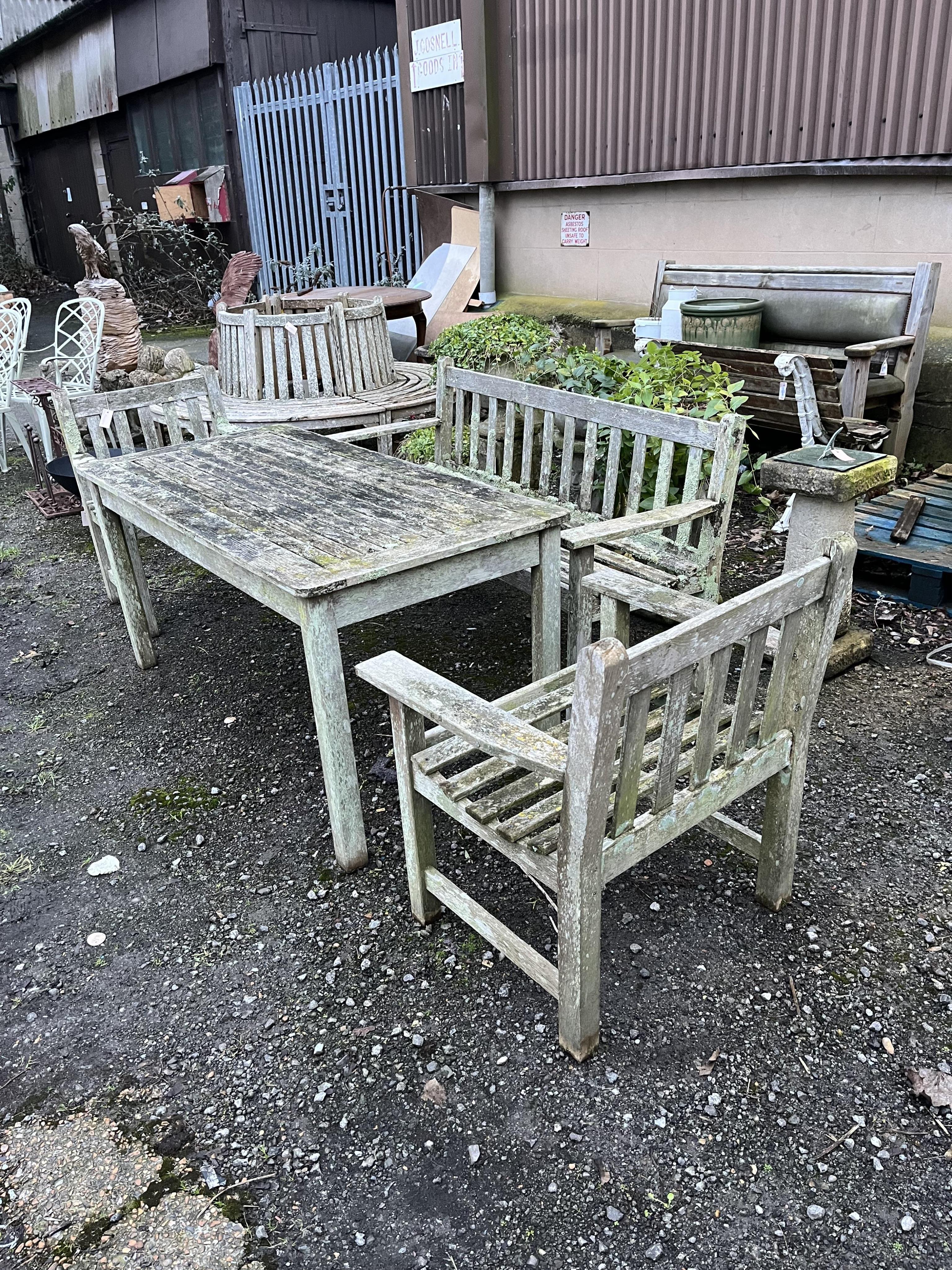 A slatted weathered teak rectangular garden table, width 149cm, depth 70cm, height 68cm, a bench and two armchairs. Condition - fair